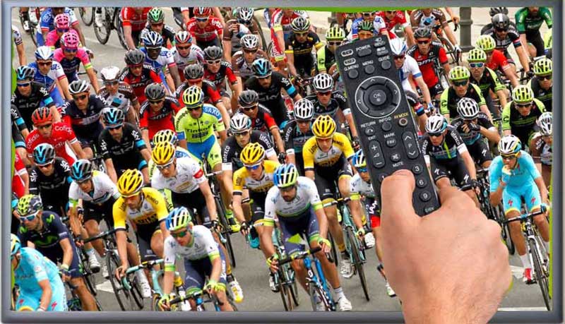 Eine Person hält eine Fernbedienung an einen Fernsehbildschirm, auf dem die Tour de France gezeigt wird.